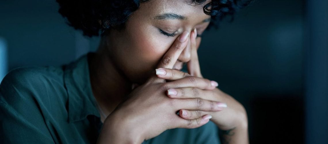 woman sitting on a work desk, head bowed, looking burnout stressed